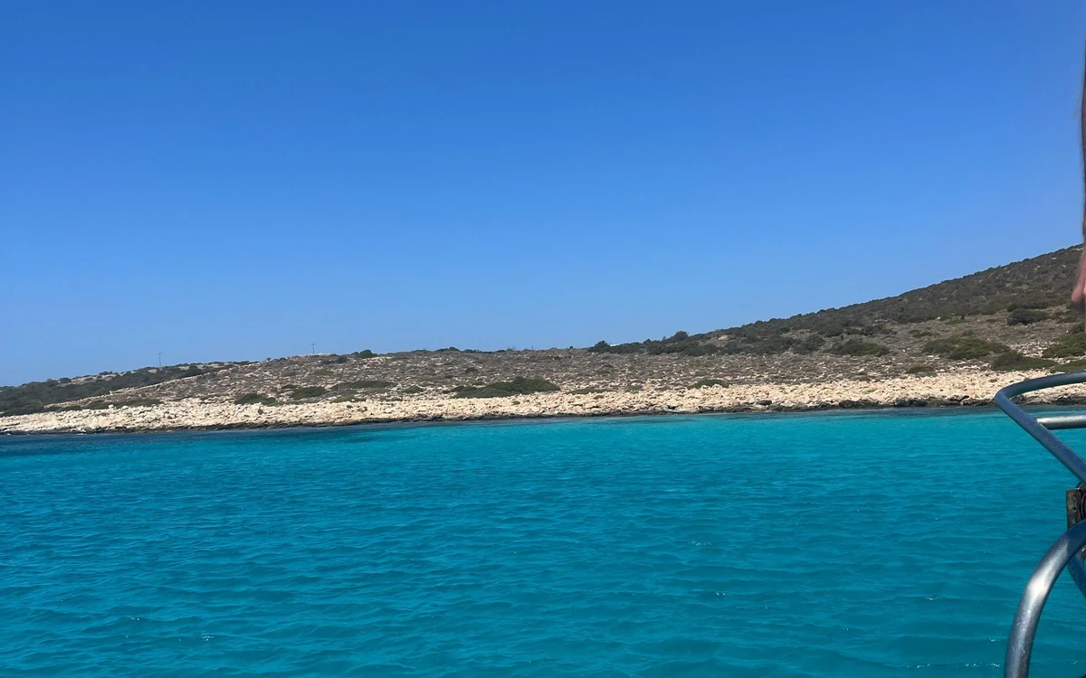 Turquoise water off a low, stony shore of Antiparos, seen from the rail of a boat