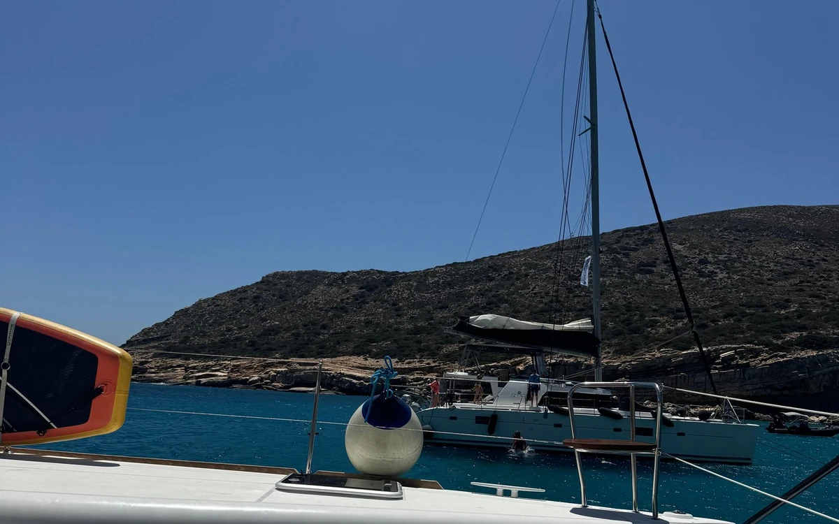 A catamaran moored in a deep blue bay below a dry hill, a paddle board on the deck in front