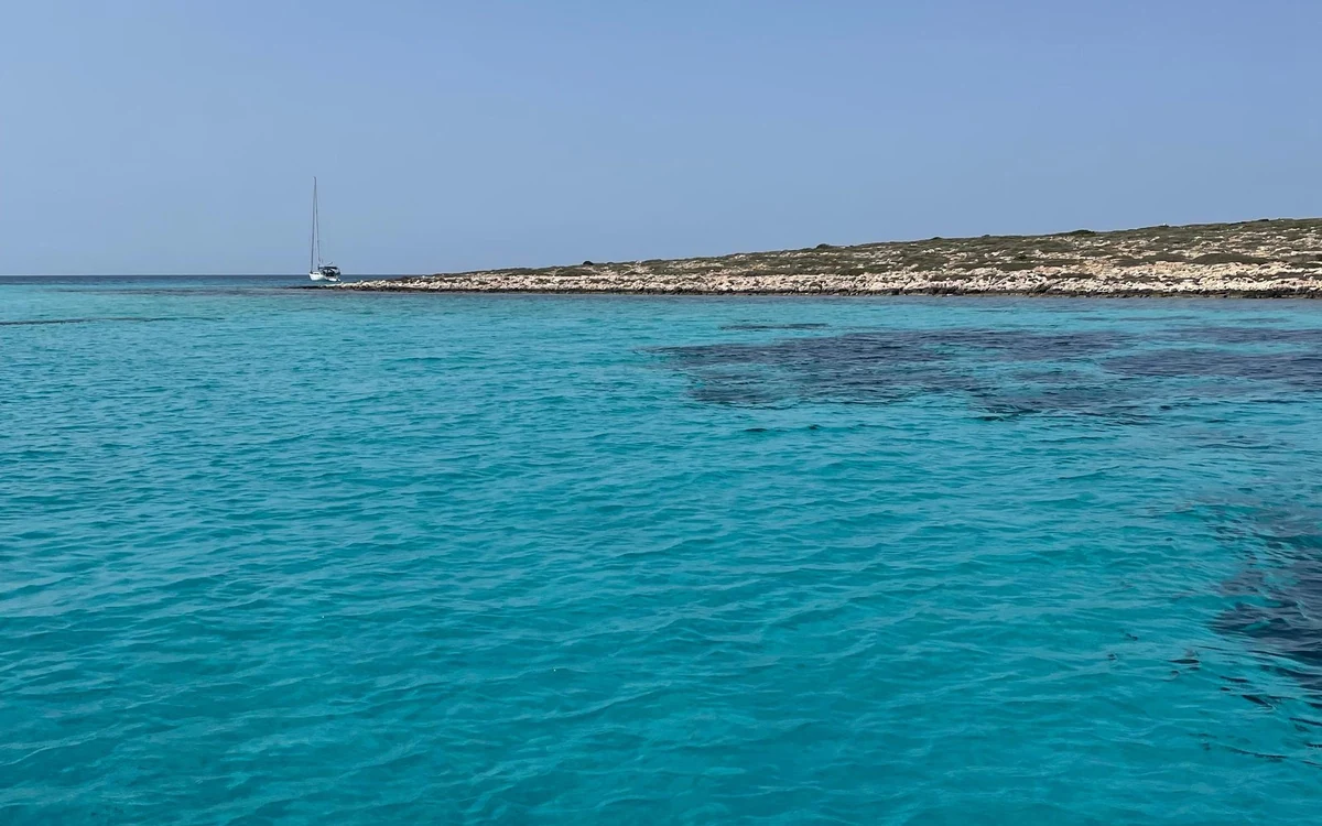 Clear turquoise shallows seen from a boat, with a low island beyond