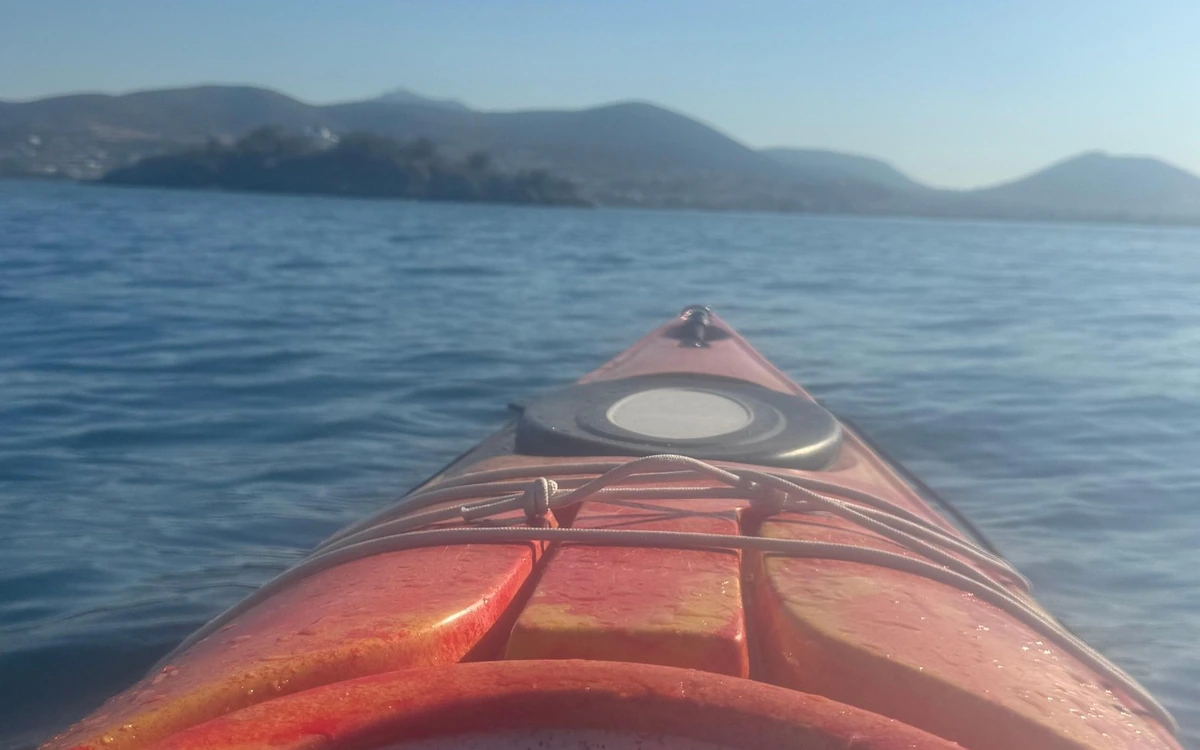 The red bow of a sea kayak on blue water with hills ahead