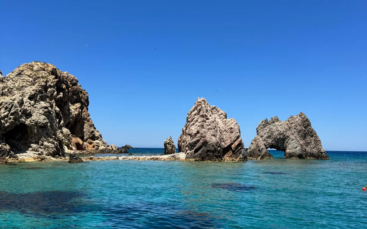 Rock stacks and a natural arch standing in turquoise water off the coast
