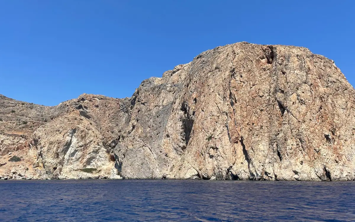A tall rocky island rising straight out of deep blue water, seen from a boat
