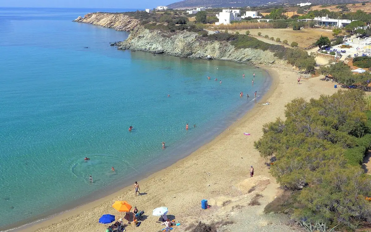 A curved sandy beach with swimmers and umbrellas, seen from the cliff above