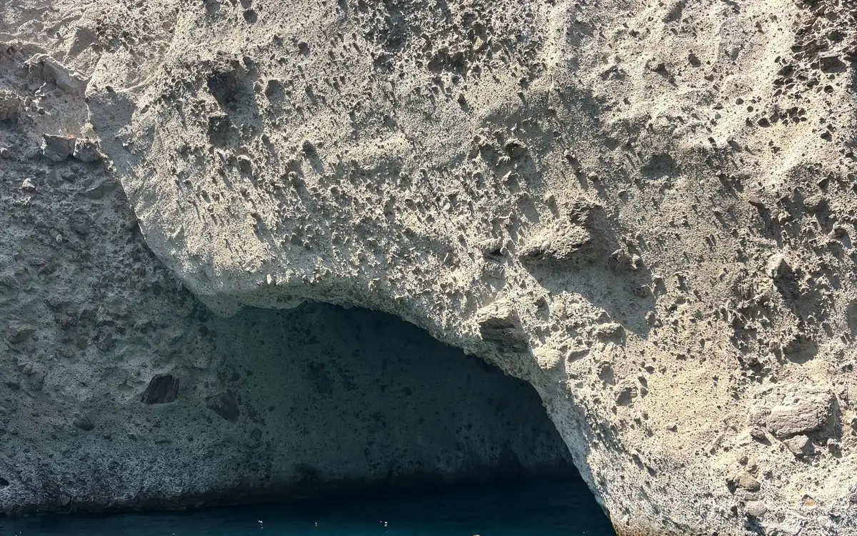 A sea cave opening in pale, pitted rock, dark blue water at its mouth