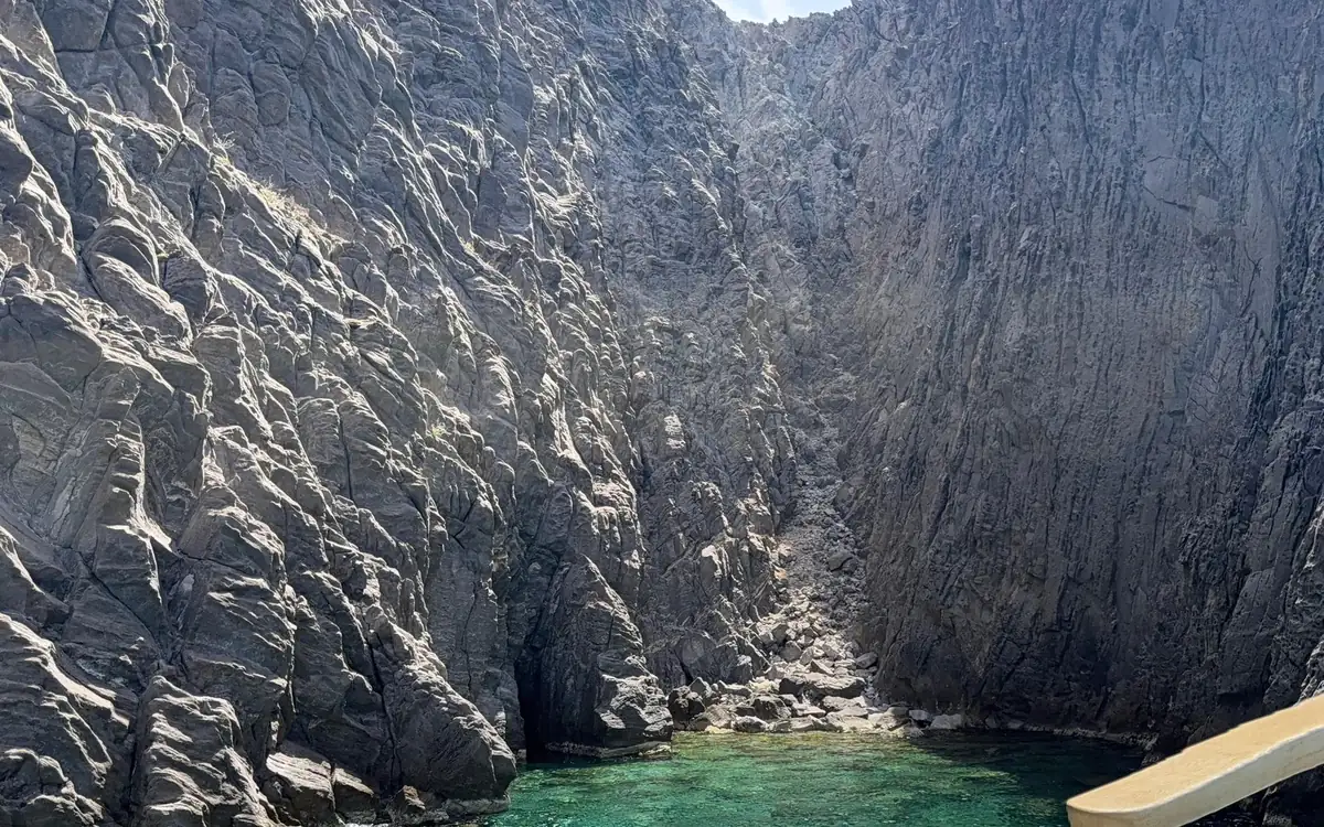 Grey cliffs closing around a pool of green water, the bow of a boat in the corner