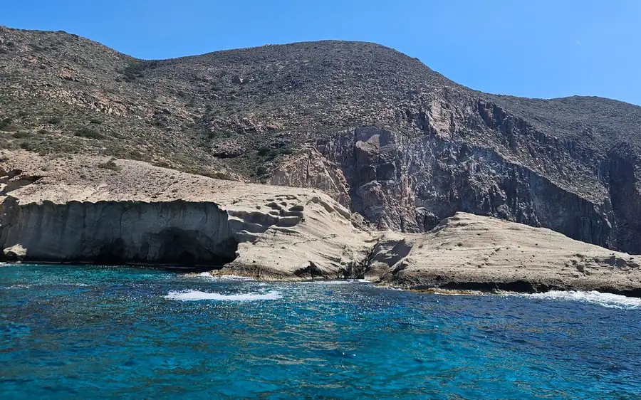 Pale rock ledges below a steep hillside, above deep blue water