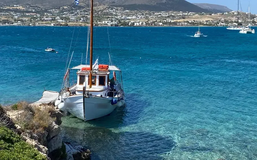 A traditional wooden boat moored by the rocks in a turquoise bay, a town behind