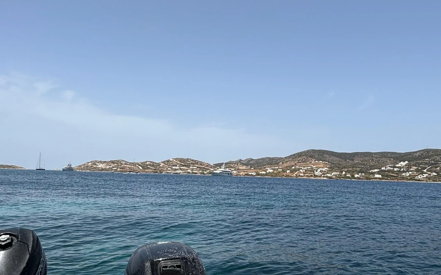 The view over the bow of a small boat towards a low coast with white houses