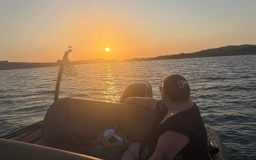 A guest at the stern of a small boat as the sun goes down