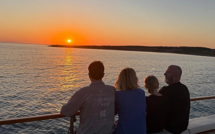 Four people at the rail of a boat watching the sun set over the sea