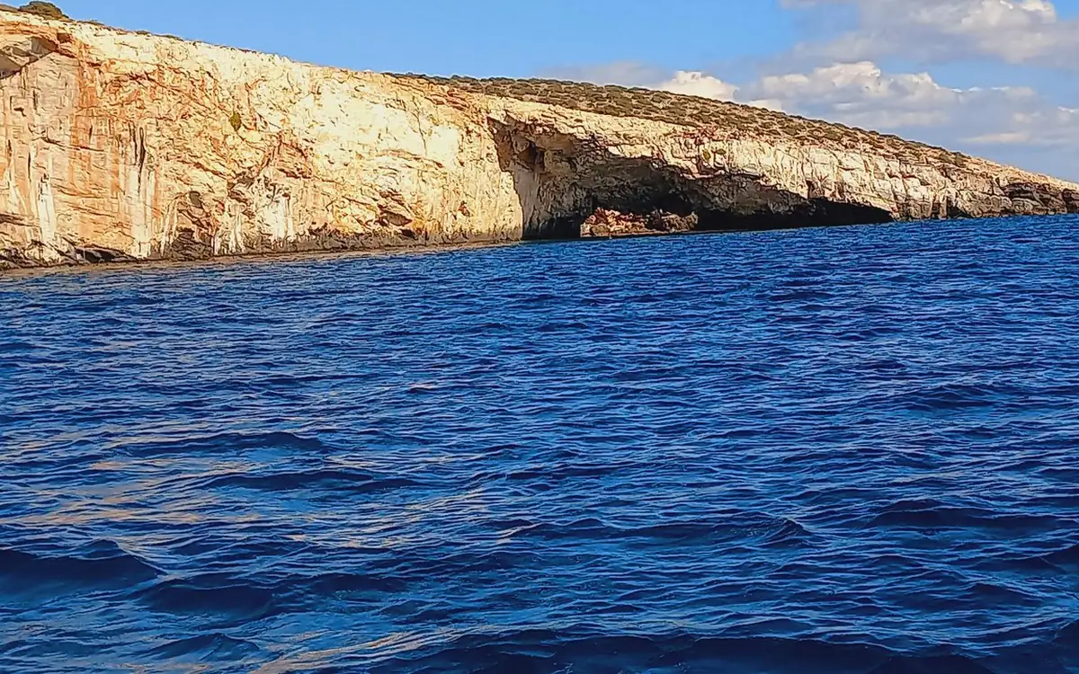 Pale cliffs with a cave at the waterline above deep blue sea
