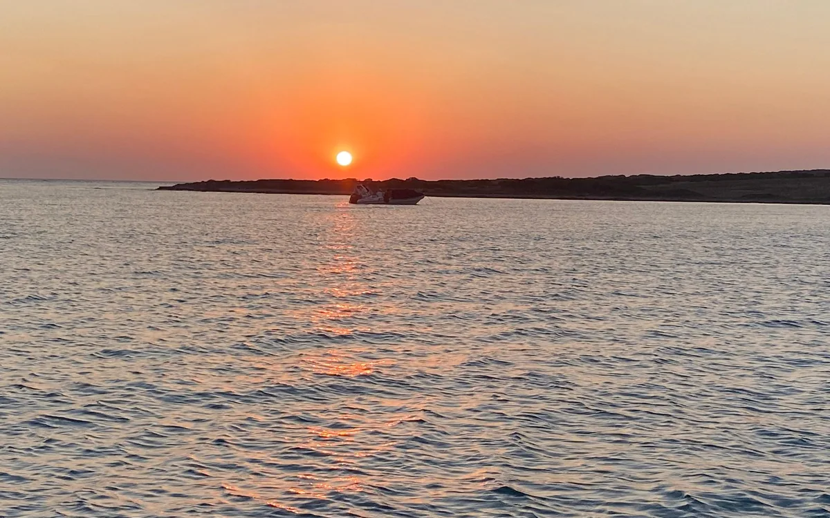 The sun setting over a low island, with a boat on the water