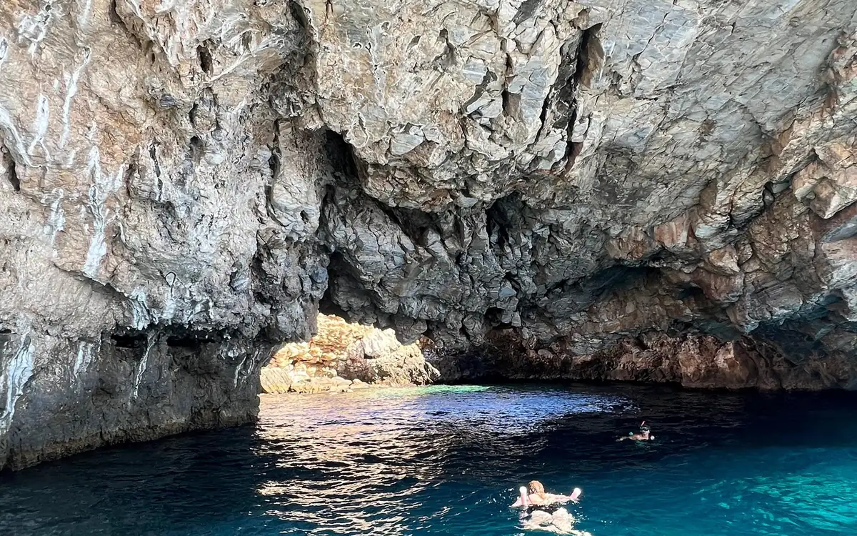 Two swimmers making their way into a wide sea cave, the water deep blue under the rock