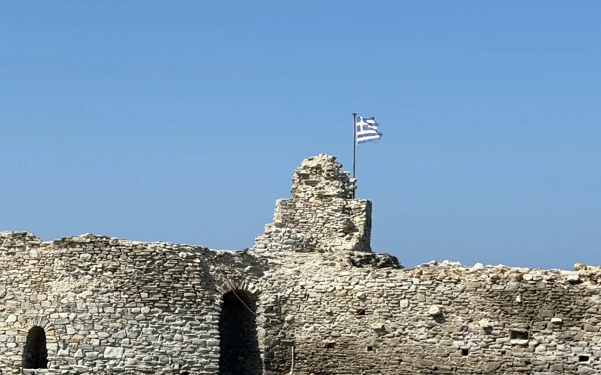 Old stone walls of a castle with the Greek flag above them