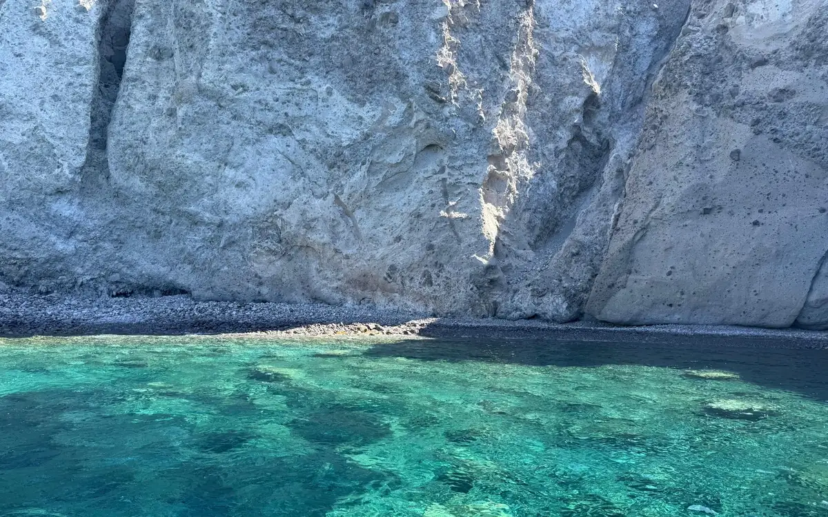 Pale cliffs above a pebble shore, turquoise water over rocks in front