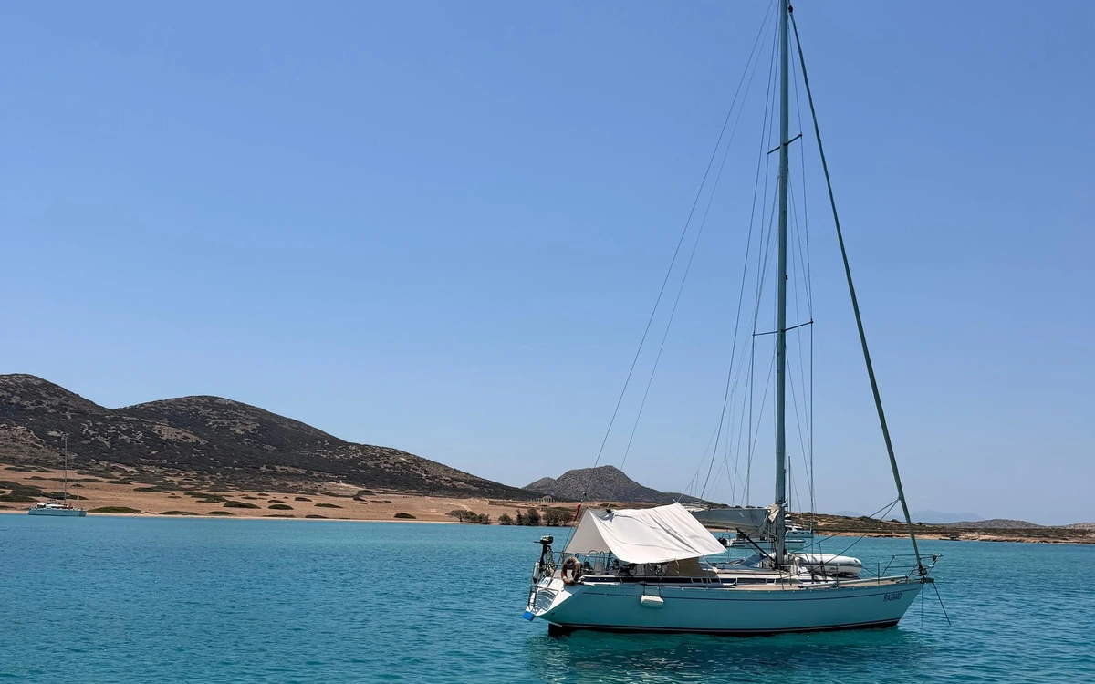 A sailing yacht at anchor in turquoise water, low brown hills behind it